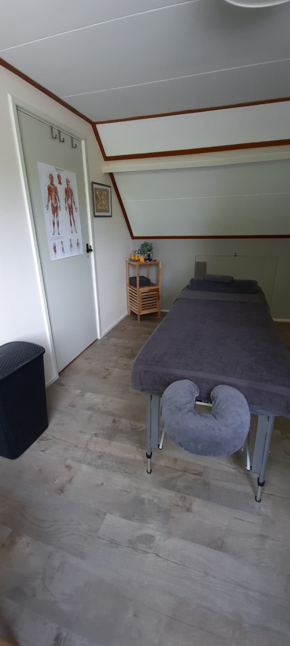 Massagetafel met hoofdsteun bij de deur, met een spierposter aan de wand